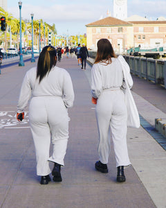 The two young women, Taysia and Kiara, Asian and Black, are walking down the Pier with their backs to the camera. They are wearing the Fog Grey colored Wide Leg Pants and Cropped Sweatshirt with black shoes.