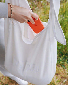 Taysia, a young woman, is wearing the Fog Grey colored Sweatshirt, with bracelet, and about to putting her orange phone in the tote bag. 